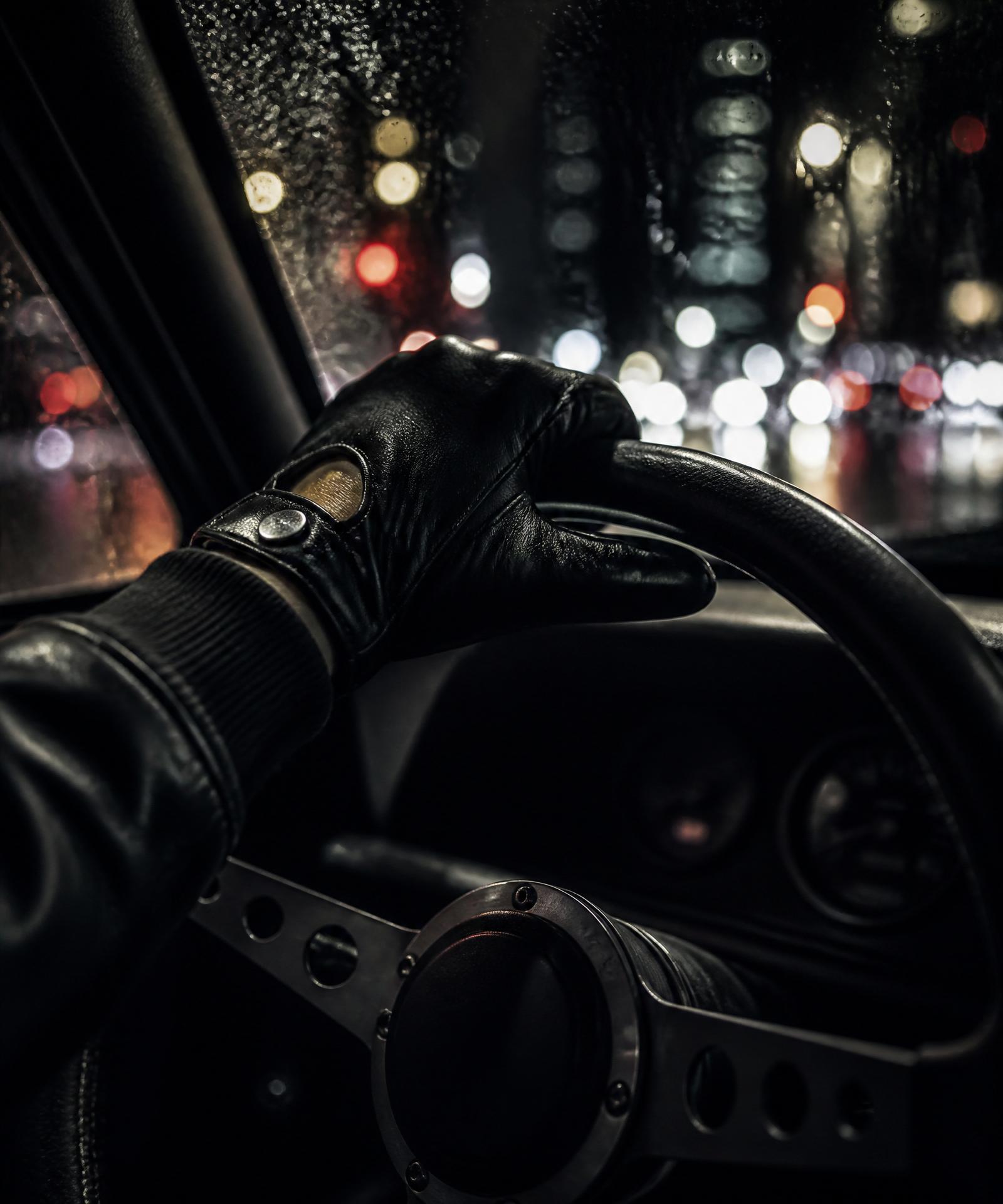 Gloved hand on steering wheel, city lights blurring through the windshield