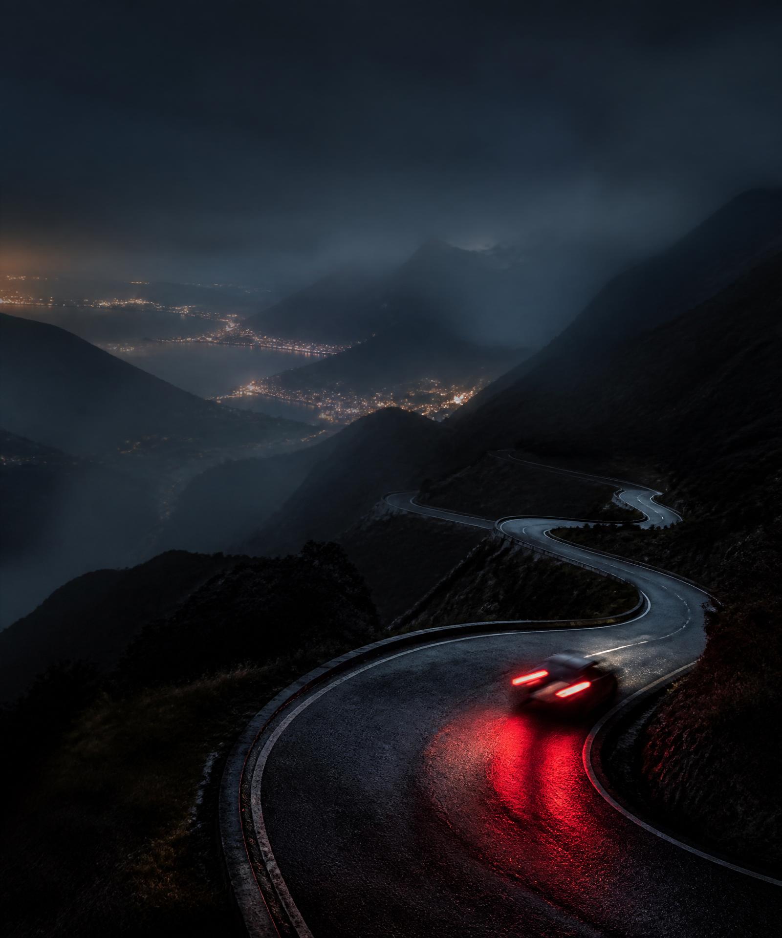 Mountain switchbacks at night, red taillights streaking through fog